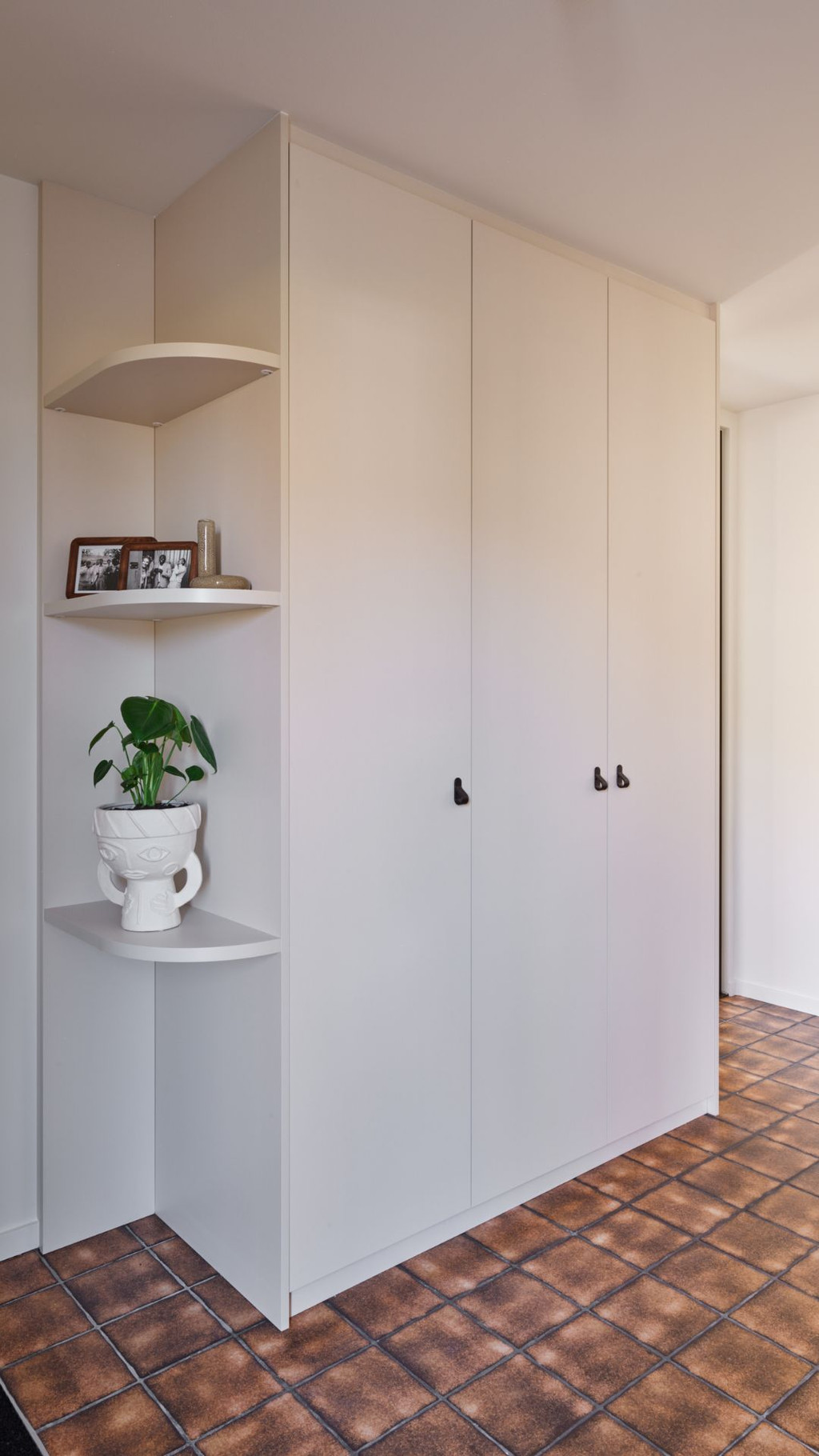 Armoire vestiaire blanche sur mesure avec niches arrondies dans un hall d’entrée avec carrelage brun