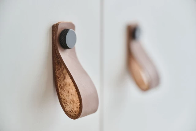 Détail de poignée en cuir avec boucle et bouton, fixée sur une porte de meuble moderne.