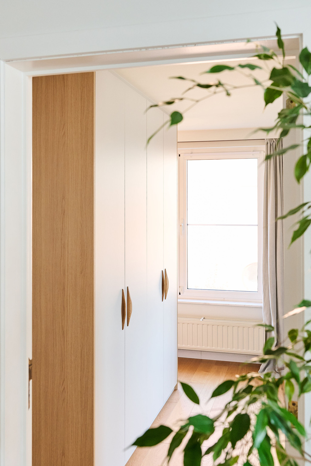 Maatkast met deuren in lichte tinten en een houten zijpaneel, geïntegreerd in een doorgang voor een discrete en elegante ruimtebenutting