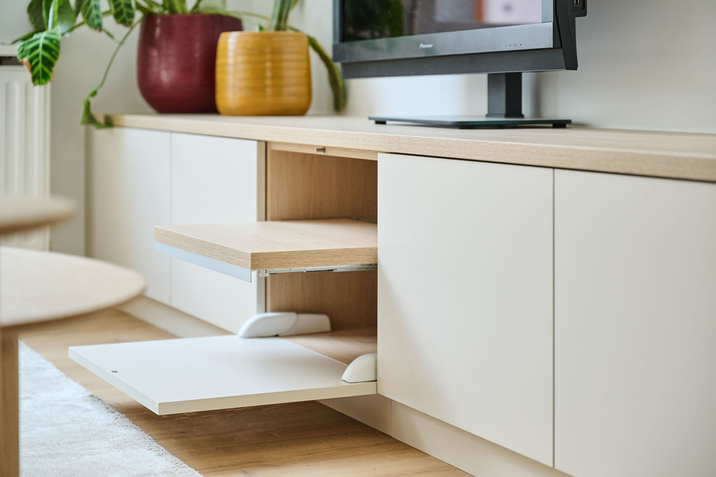 Détail d’un meuble TV avec portes abattantes et tablette coulissante en bois clair