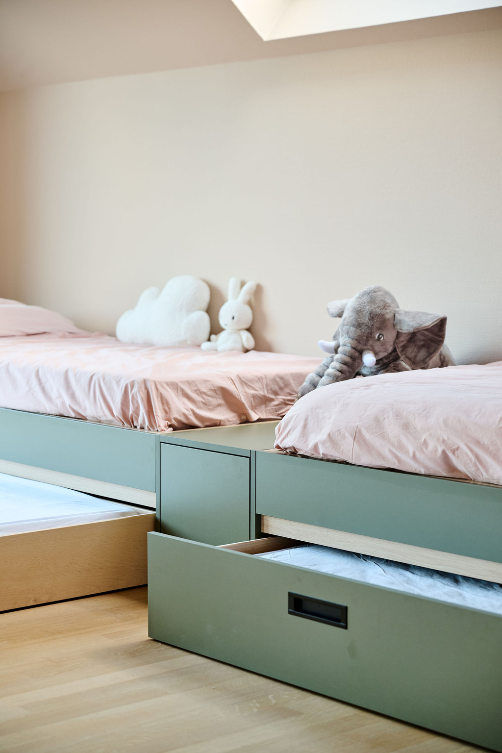 Deux lits verts sur mesure avec tiroirs ouverts et peluches posées sur la literie rose