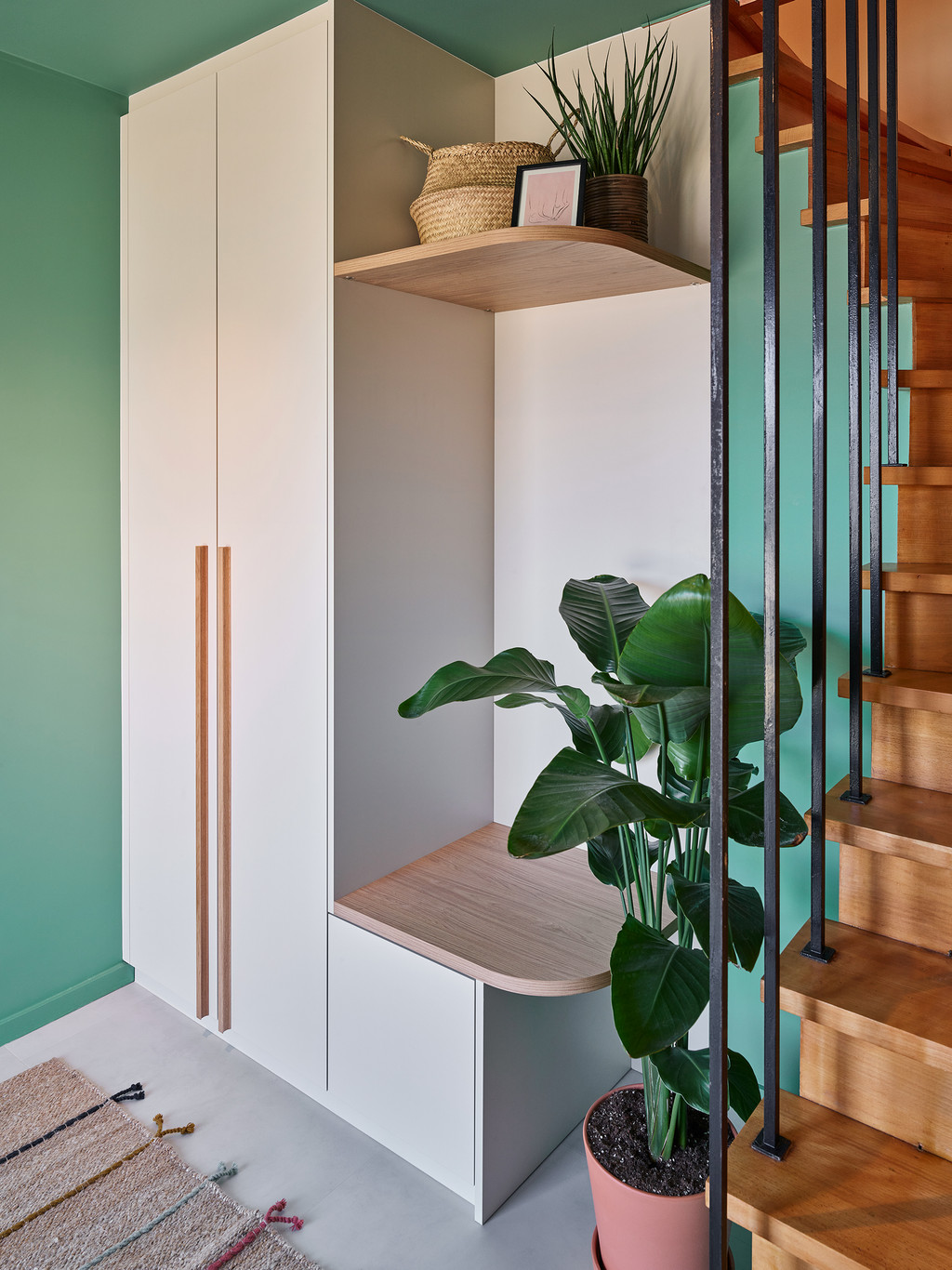 Zijaanzicht van witte vestiaire op maat met houten zitbankje en groene plant naast trap