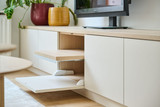Détail d’un meuble TV avec portes abattantes et tablette coulissante en bois clair