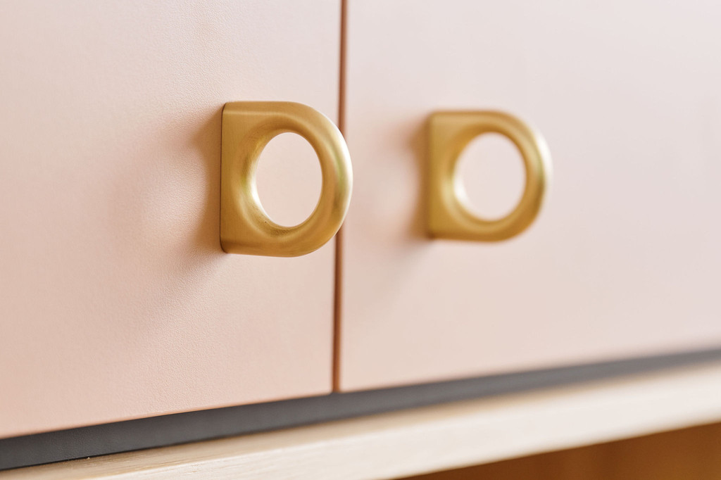 poignées dorées arrondies fixées sur des portes de placard rose pâle avec un socle en bois clair.