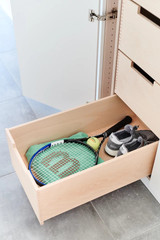 Ingetrokken lade in een kast met sportaccessoires zoals een rackets en sportschoenen.