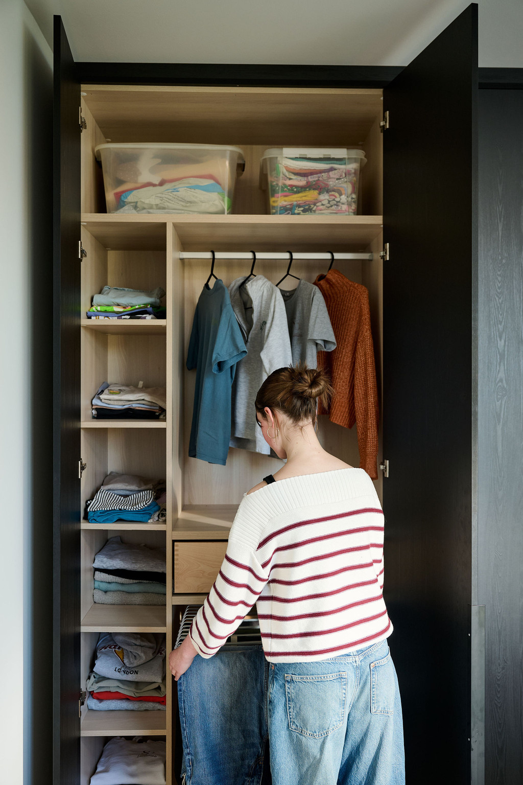 Penderie ouverte sur mesure avec portes noires, étagères, tringle et porte-pantalons coulissant, femme sort un jean