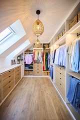 Dressing op maat onder een schuin dak met hangruimte, lades en open legplanken, voor een optimale benutting van de ruimte, gerealiseerd door Camber