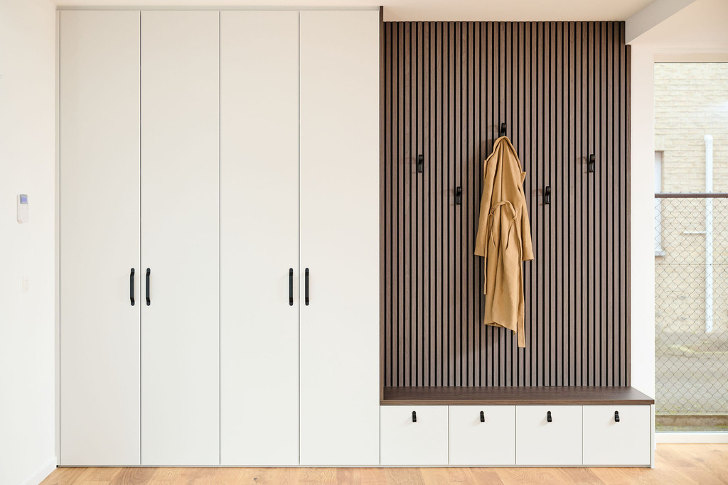 Witte vestiairekast op maat met zwarte handgrepen en een houten lattenwand met kapstokken en een zitbank met opberglades.