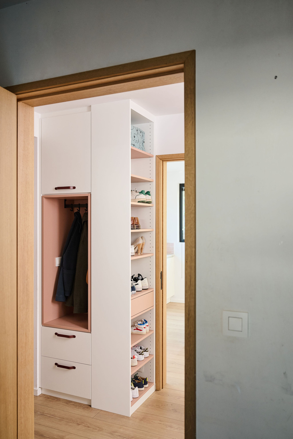 Vestiaire Camber sur mesure avec niche ouverte pour manteaux, tiroirs intégrés et rangement à chaussures ouvert, visible depuis le passage vers l’espace de vie et réalisée dans des tons clairs avec des accents en bois