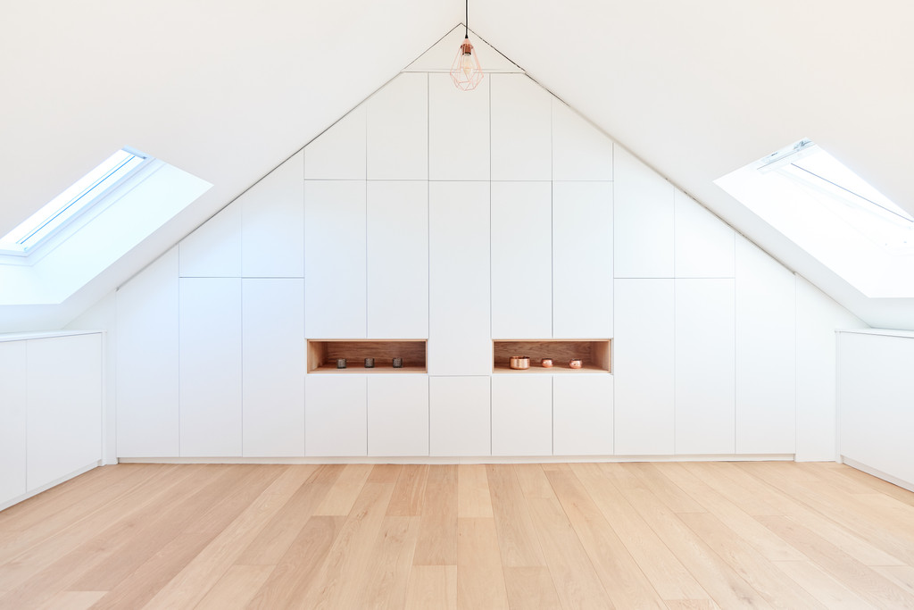 Op maat gemaakte dressing onder een schuin dak met witte fronten, geïntegreerde houten niches en natuurlijk licht.