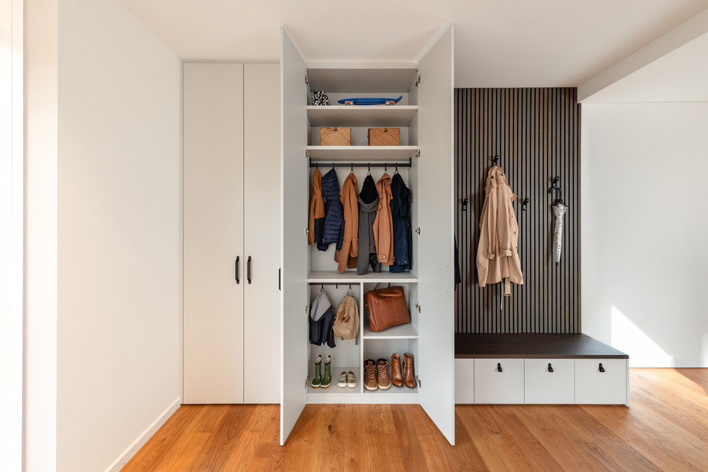 Moderne vestiairekast op maat met open en gesloten deuren, kledingroede, schoenenvakken en geïntegreerde zitbank met wandhaken.