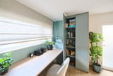 Open maatwerkkast in blauw bureau met boeken en decoratie naast werkblad aan raam in lichte ruimte