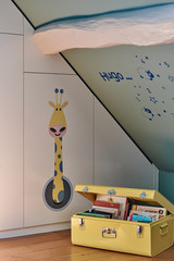 Détail d'une décoration murale d'une girafe et étagères avec des livres dans une chambre d'enfant.