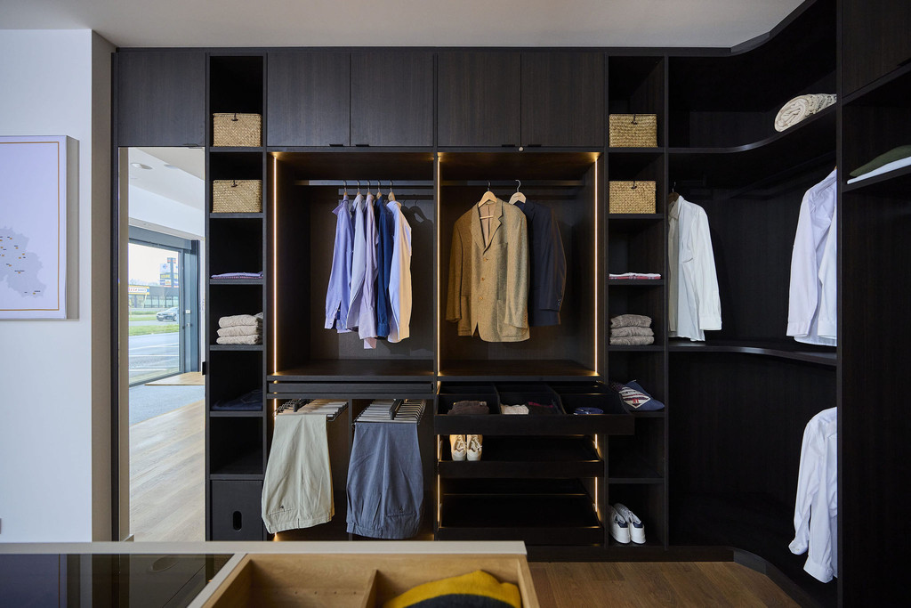 Dressing sur mesure avec penderie, tiroirs et niches ouvertes en bois foncé dans un showroom