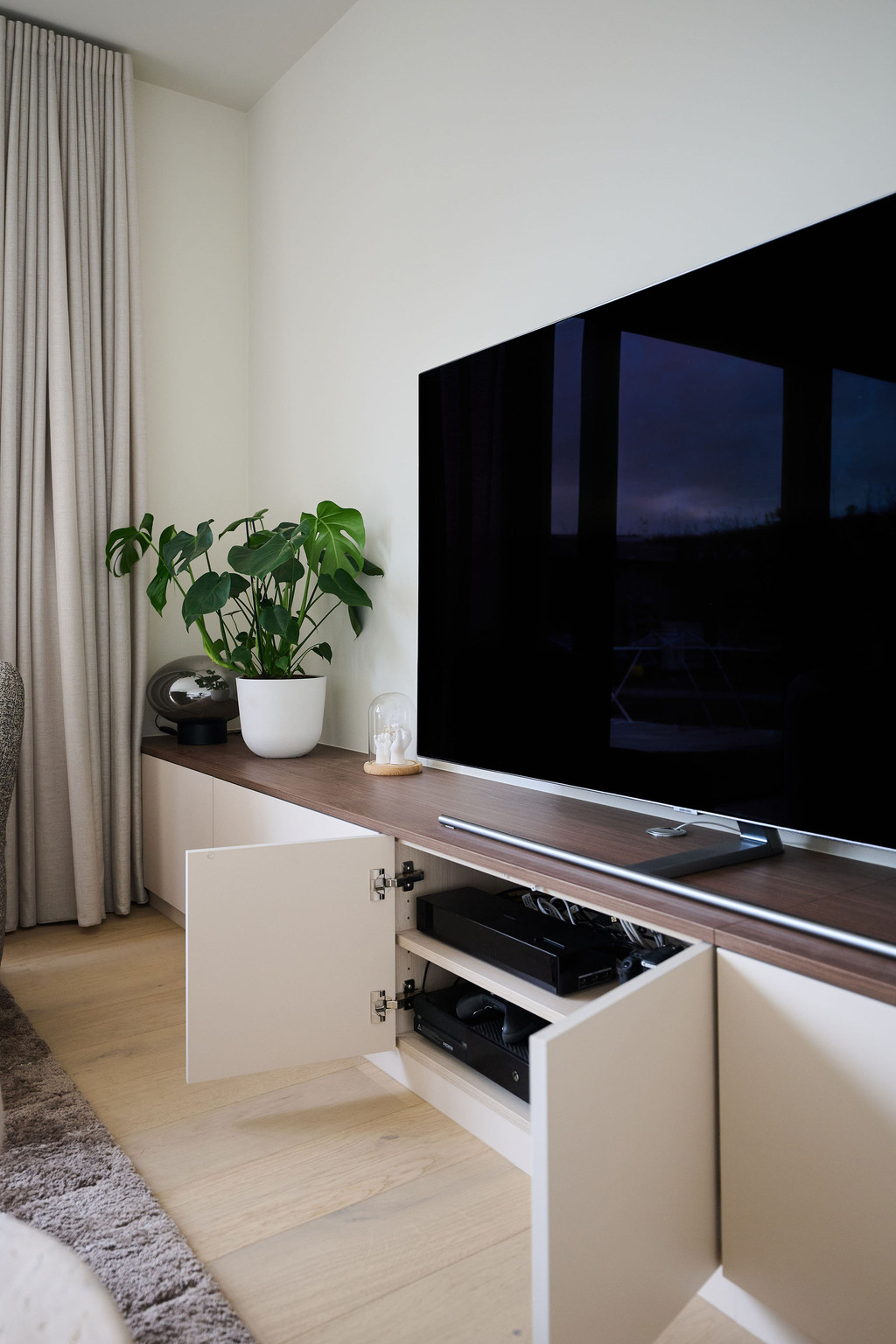 Meuble télé sur mesure ouvert avec rangements multimédia sous écran plat dans salon moderne