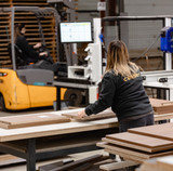 Une collaboratrice Camber manipule des panneaux de bois sur une table de travail dans l’usine de Chailley, avec un chariot élévateur en arrière-plan