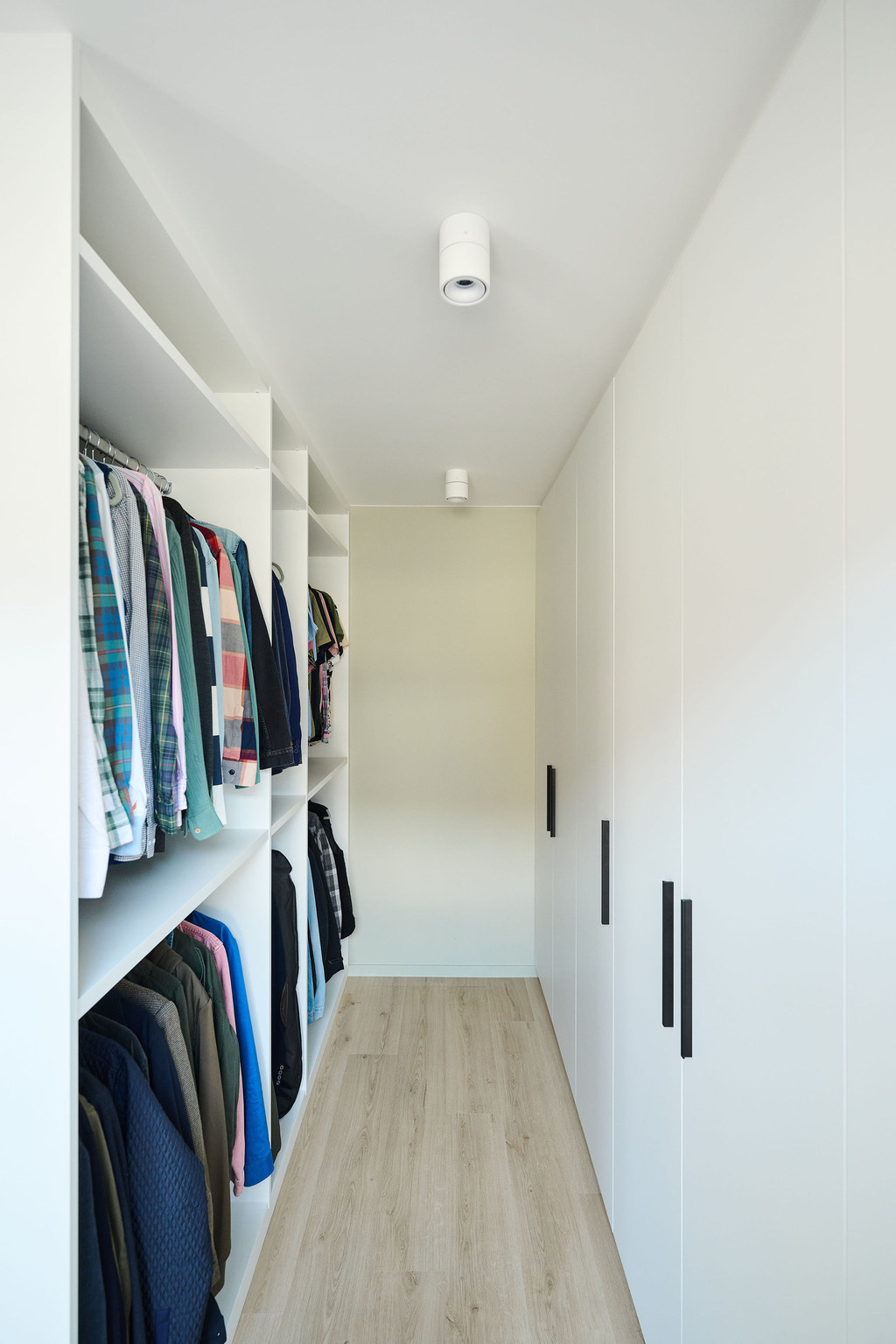 Witte dressing met open legvakken en hangruimte tegenover gesloten kastdeuren met zwarte handgrepen
