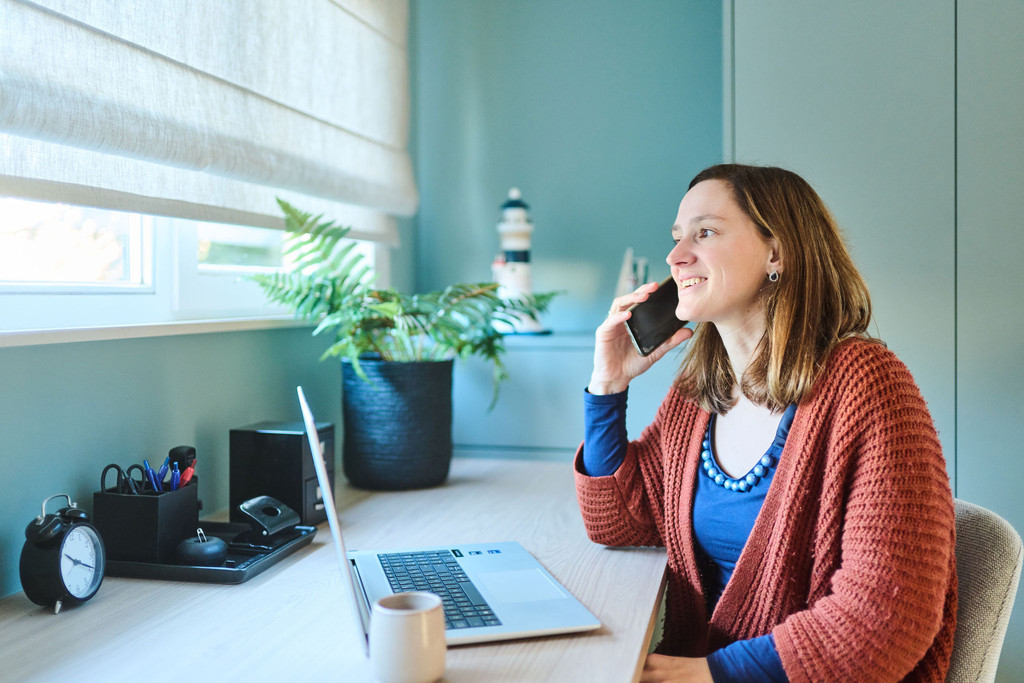 Vrouw aan bureau op maat met laptop plant en blauw kastvolume in lichtrijke werkruimte