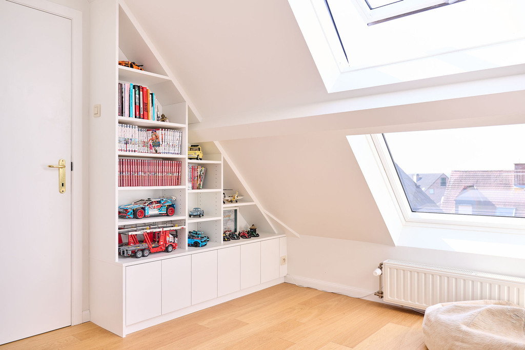 Placard bibliothèque sur mesure sous pente avec niches ouvertes pour livres et jouets dans une chambre d’enfant