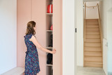 Femme ouvrant une armoire rose avec étagères dans un hall d’entrée lumineux