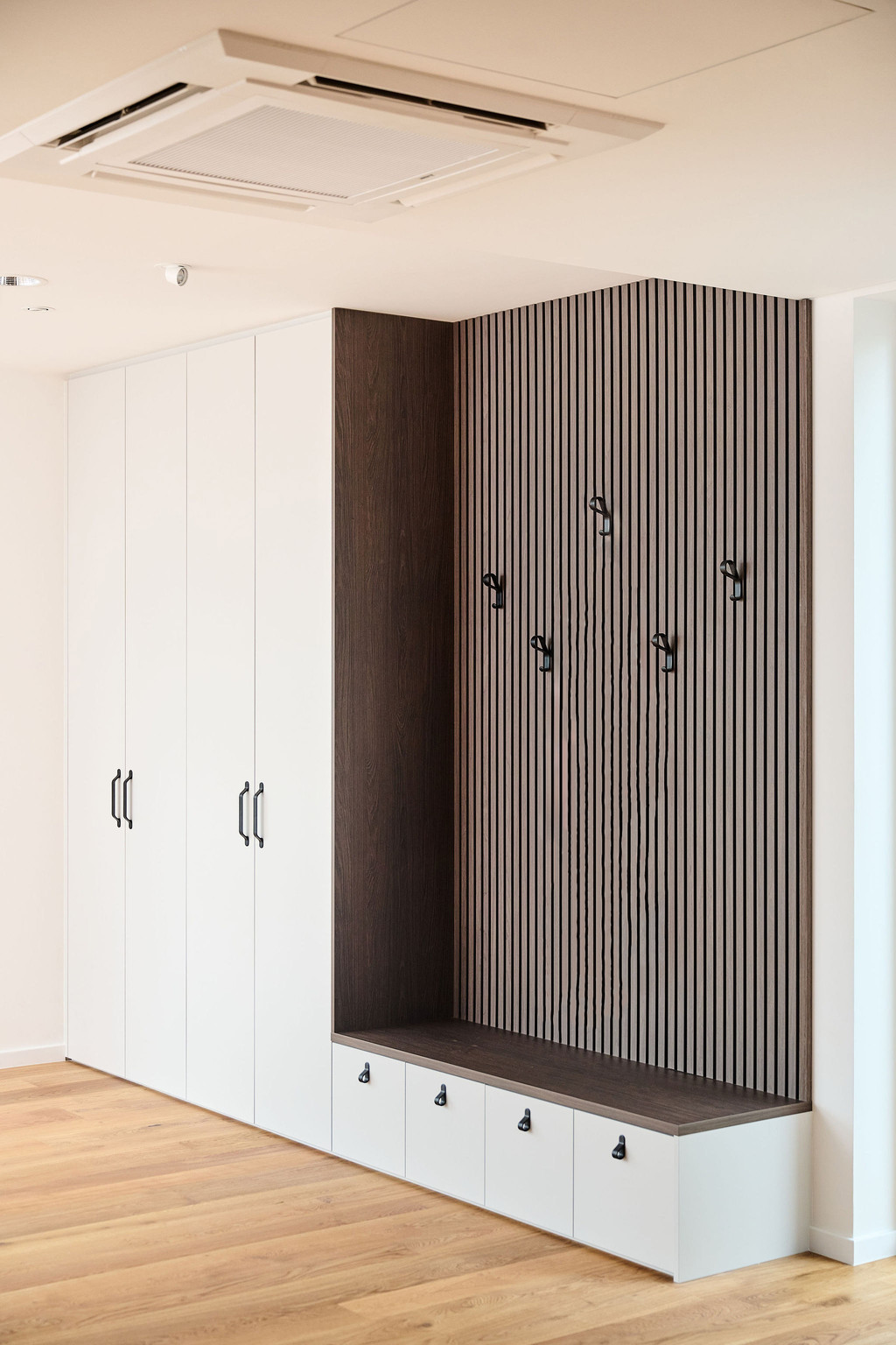 Witte vestiaire op maat met houten zitbank, zwarte haken en verticale lattenwand voor een moderne uitstraling.