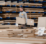 Un collaborateur Camber transporte un panneau de bois dans l’usine de Chailley, avec des panneaux empilés en arrière-plan