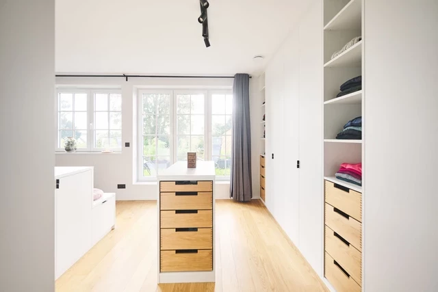 Moderne dressing op maat met witgelakte kasten en houten lades, natuurlijk verlicht.