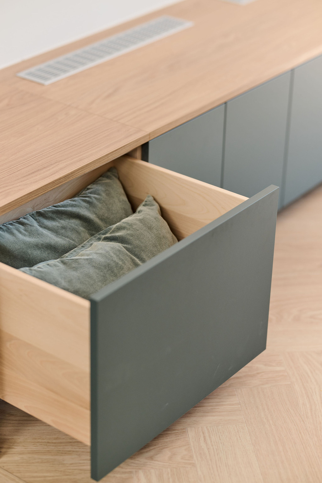Tiroir ouvert d’un meuble bas sur mesure contenant des coussins verts dans un intérieur lumineux