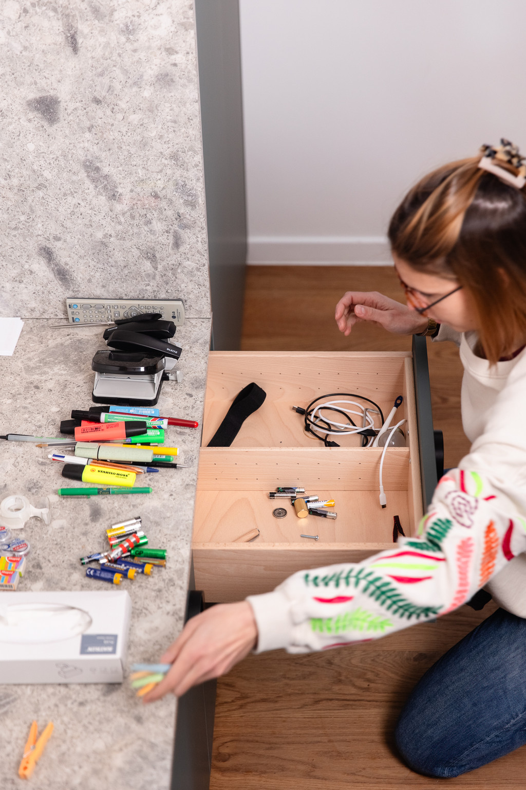 Femme organisant un tiroir sur mesure en bois, vidant les accessoires de bureau et classant les objets pour un rangement pratique.