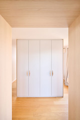 Placard sur mesure utilisé comme séparateur de pièce avec portes blanches et poignées en bois dans une chambre