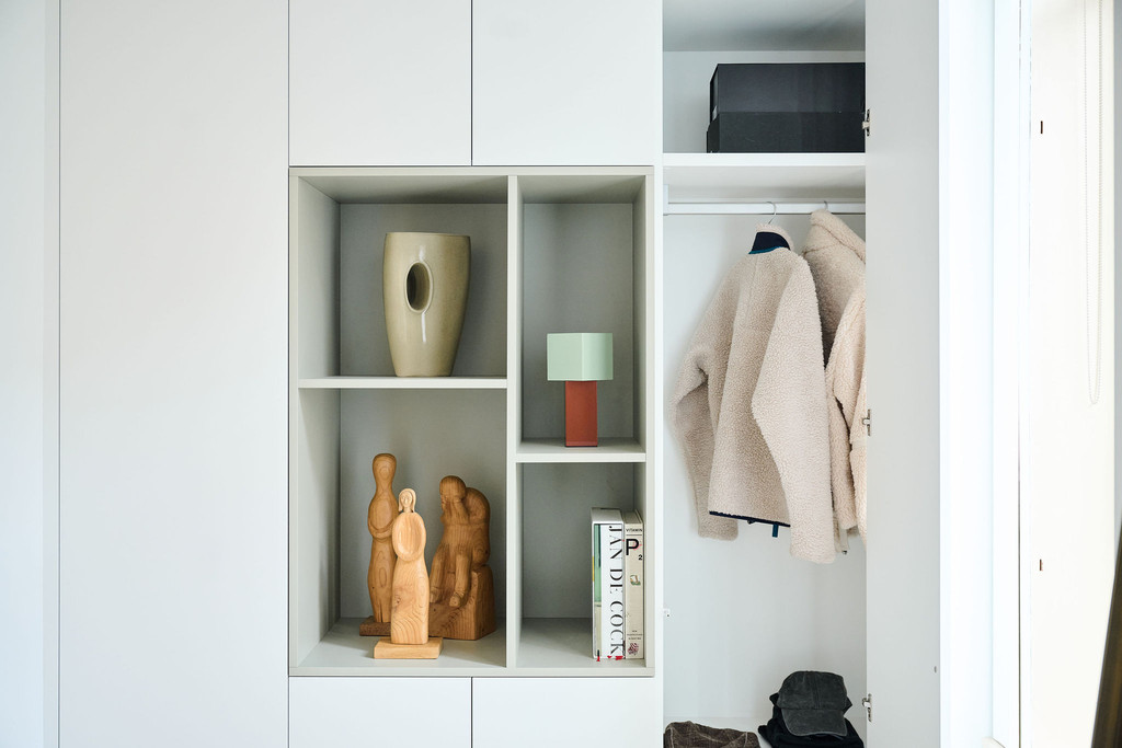 Vestiaire blanche avec niches décoratives et porte ouverte révélant manteaux chaussures et sac à main