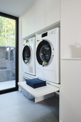Wasruimte op maat met wasmachine en opbergruimte voor wasgoed in een moderne setting met grote ramen.