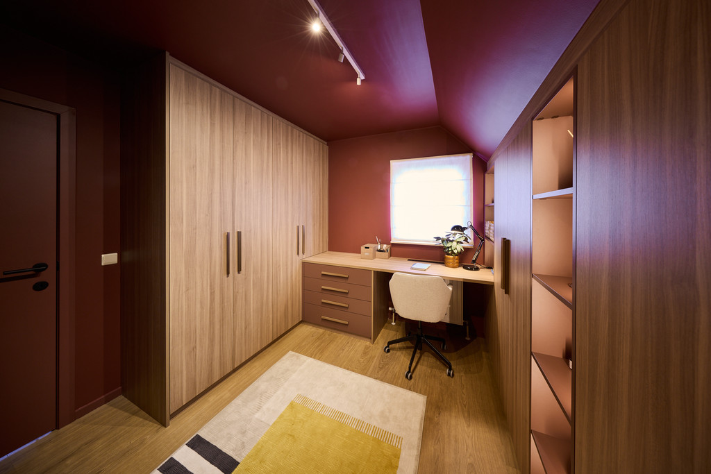 Maatkasten onder schuine wand met houten afwerking en geïntegreerd bureau in een warme slaapkamer