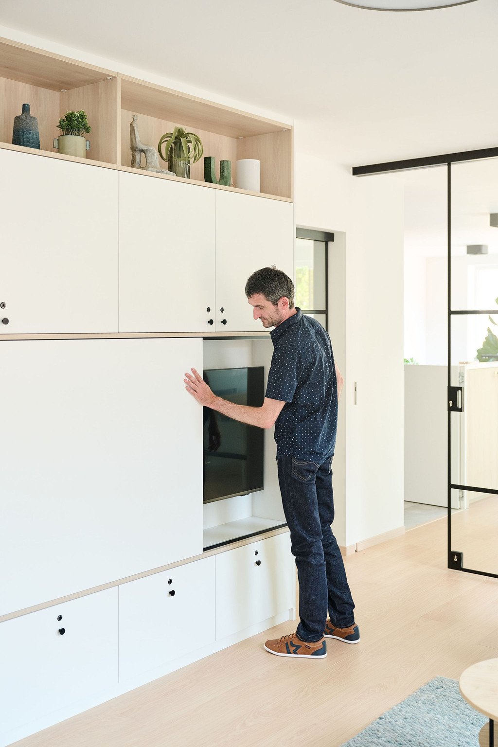 Homme ouvrant la porte coulissante d’un meuble sur mesure blanc avec niche TV dans un salon moderne