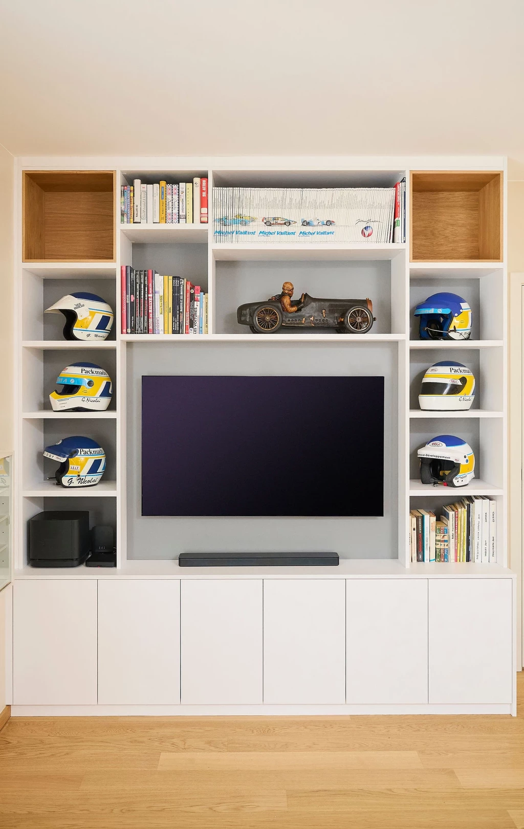 Moderne woonkamer met een op maat gemaakte tv-meubel met open vakken, boeken, helmen en een tv in het midden, onder een witte kast.