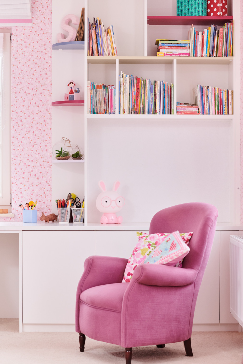Meuble de rangement sur mesure avec étagères et espace de travail pour chambre d’enfant avec fauteuil rose.