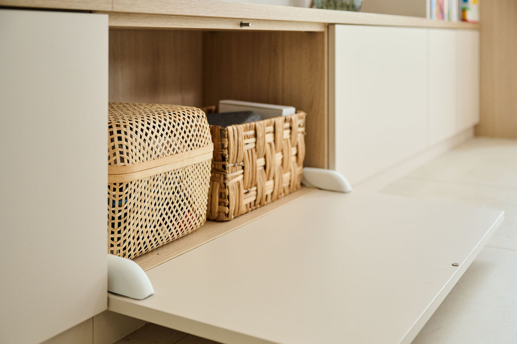 Détail d'un meuble TV sur mesure avec porte abattante, mettant en valeur des paniers en osier pour un rangement pratique et esthétique.