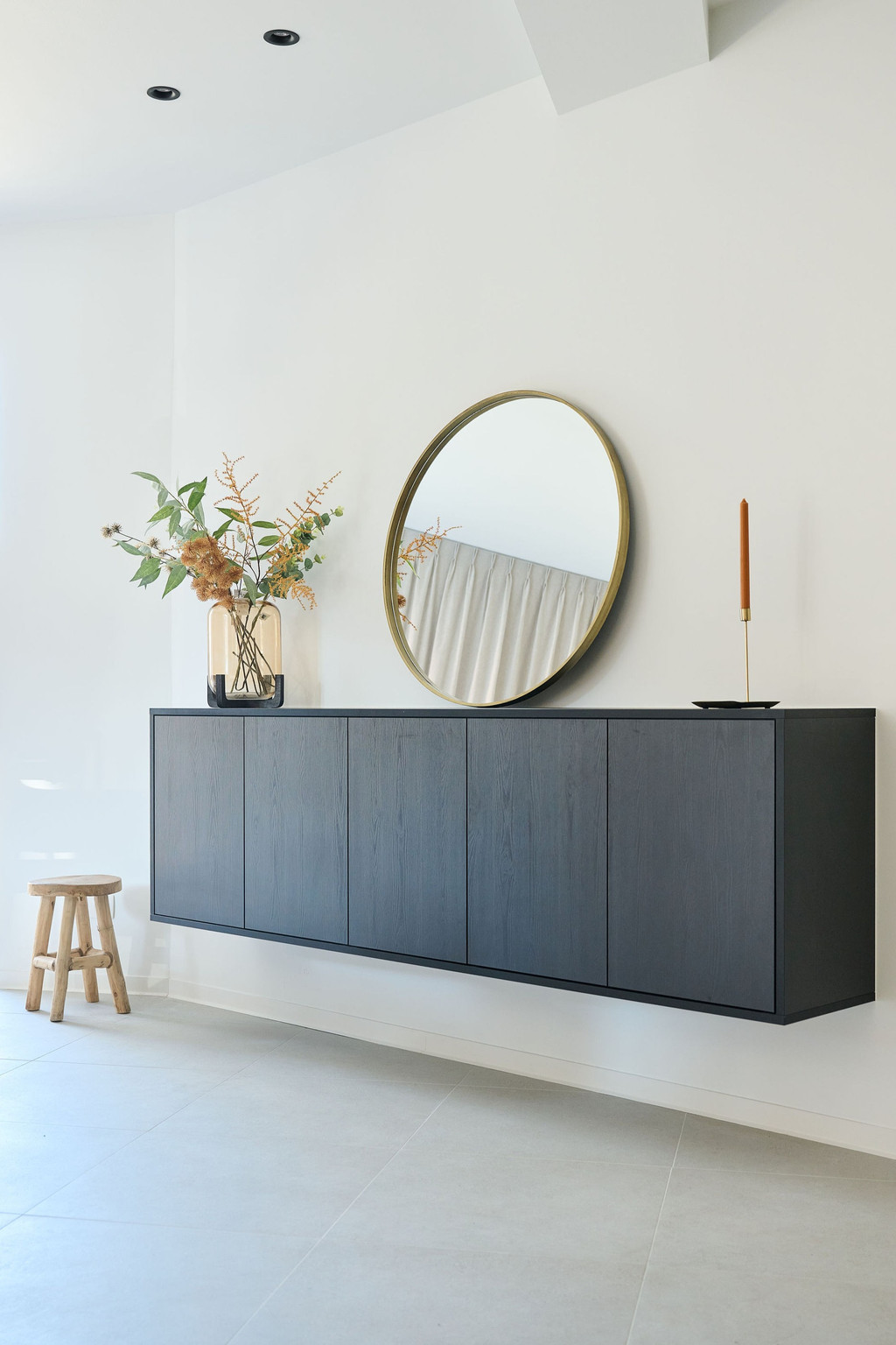 Meuble bas de salon sur mesure avec miroir rond, décoré de plantes et accessoires, dans un salon moderne.
