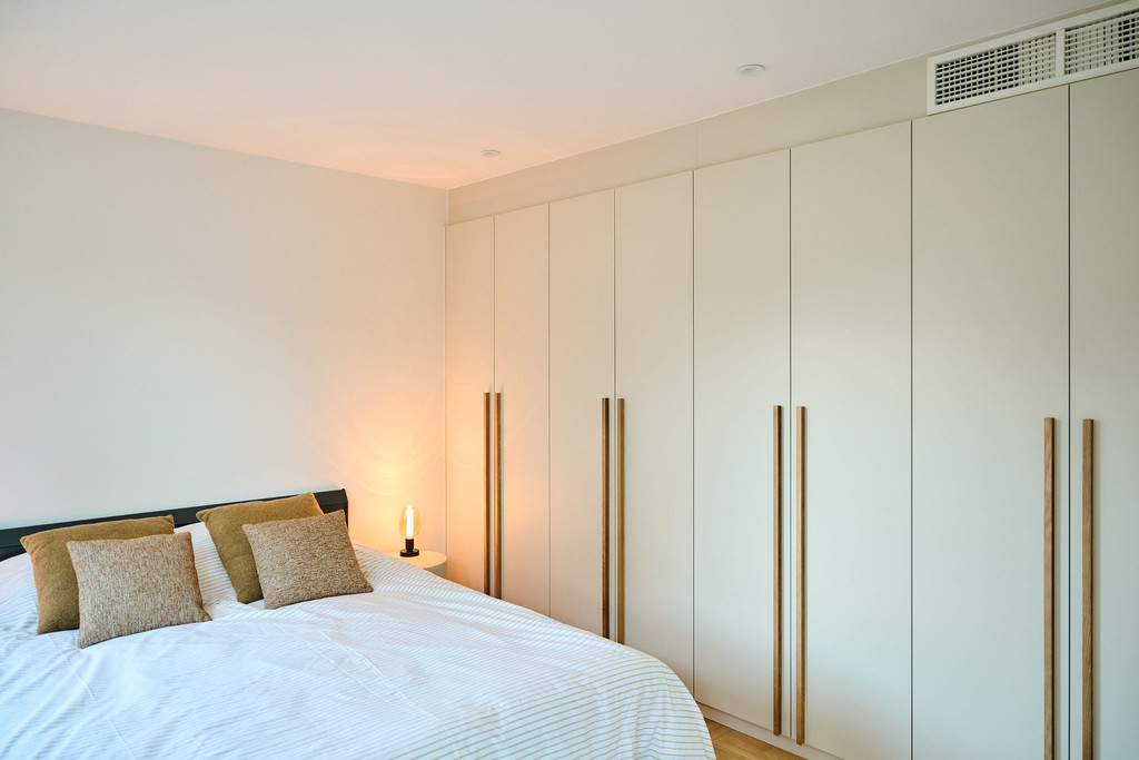 Chambre avec armoire sur mesure beige et lit double avec coussins assortis et lampe d’appoint