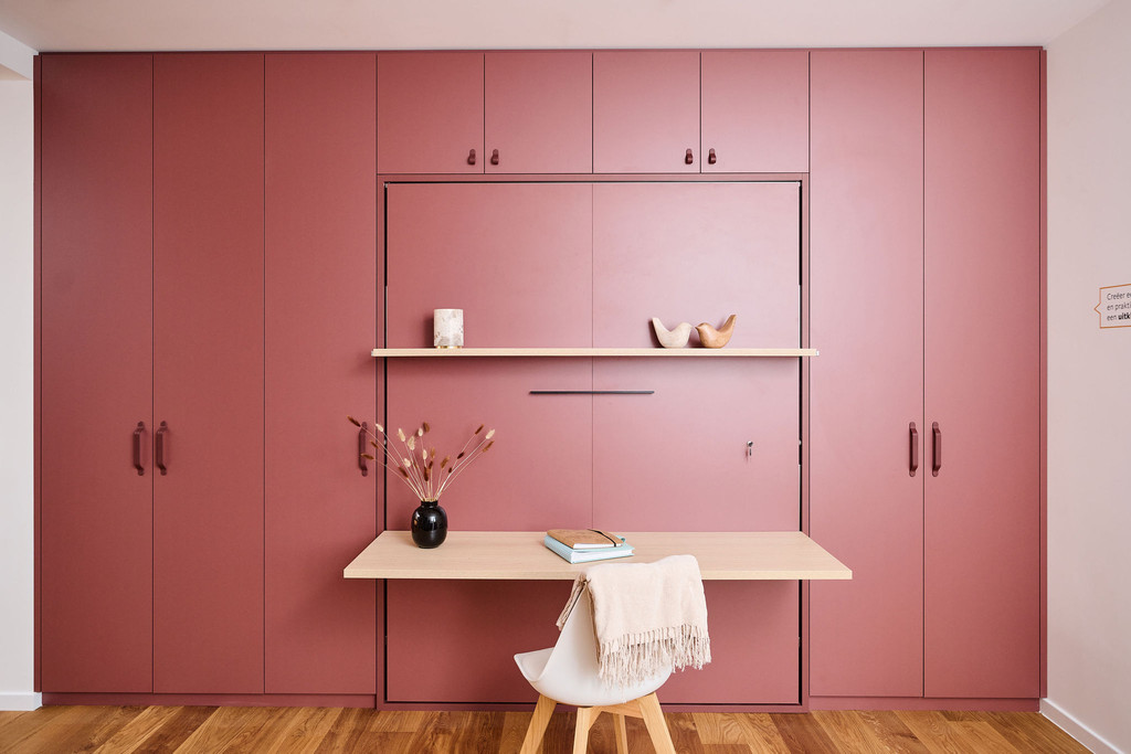 Bureau sur mesure avec table rabattable et étagère en bois, décoré de vase et de fleurs, dans une pièce avec des murs roses.
