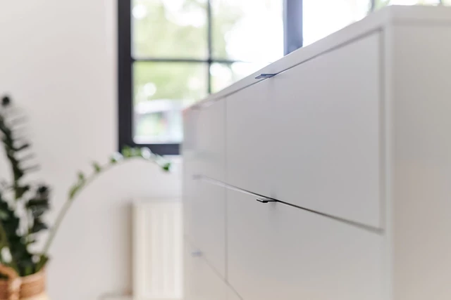 Détail d’un îlot de dressing blanc avec poignées modernes et fines pour une finition épurée