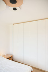 Witte kledingkast op maat van vloer tot plafond in een slaapkamer met greeploze deuren en een subtiele houten omlijsting
