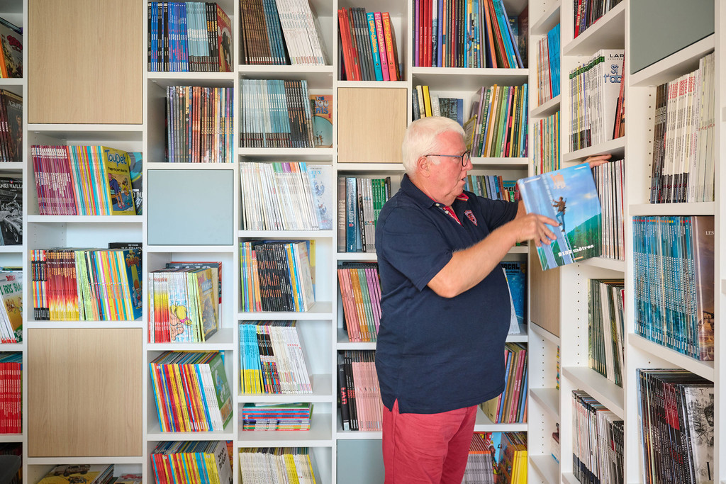 Guido neemt een boek uit een wandvullende bibliotheekkast op maat met open vakken en gesloten opbergvakken